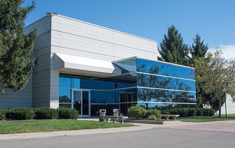 Large glass and steel commercial building flanked by tall green trees.